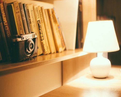 A close up of a soft glowing modern ceramic desk lamp next to books